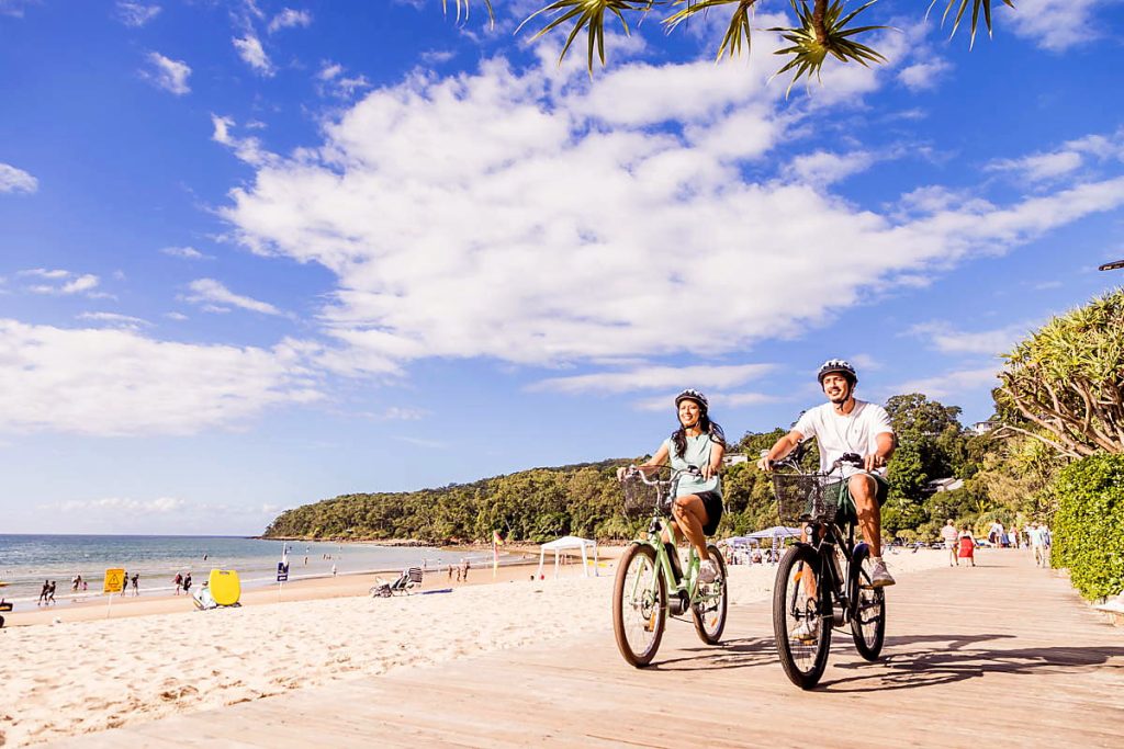 Couple riding e-Bikes along the beachfront path in Noosa