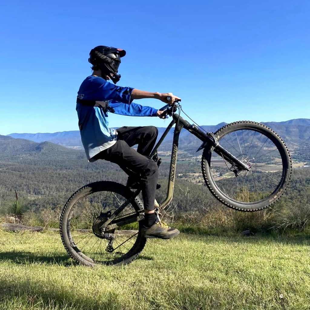 Rider pulling a wheelie at a hinterland lookout with the mountains behind