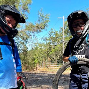 Two young riders in full face helmets with their bikes at the trailhead