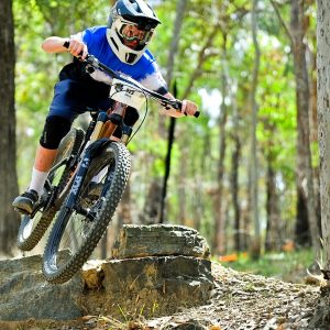 Young rider in a full face helmet rolling off a rock drop on a forest trail