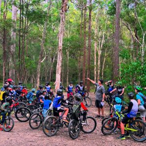 Large group of kids on bikes listening to a coach in the forest
